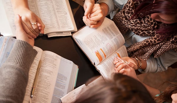 Women holding hands and praying over the Bible